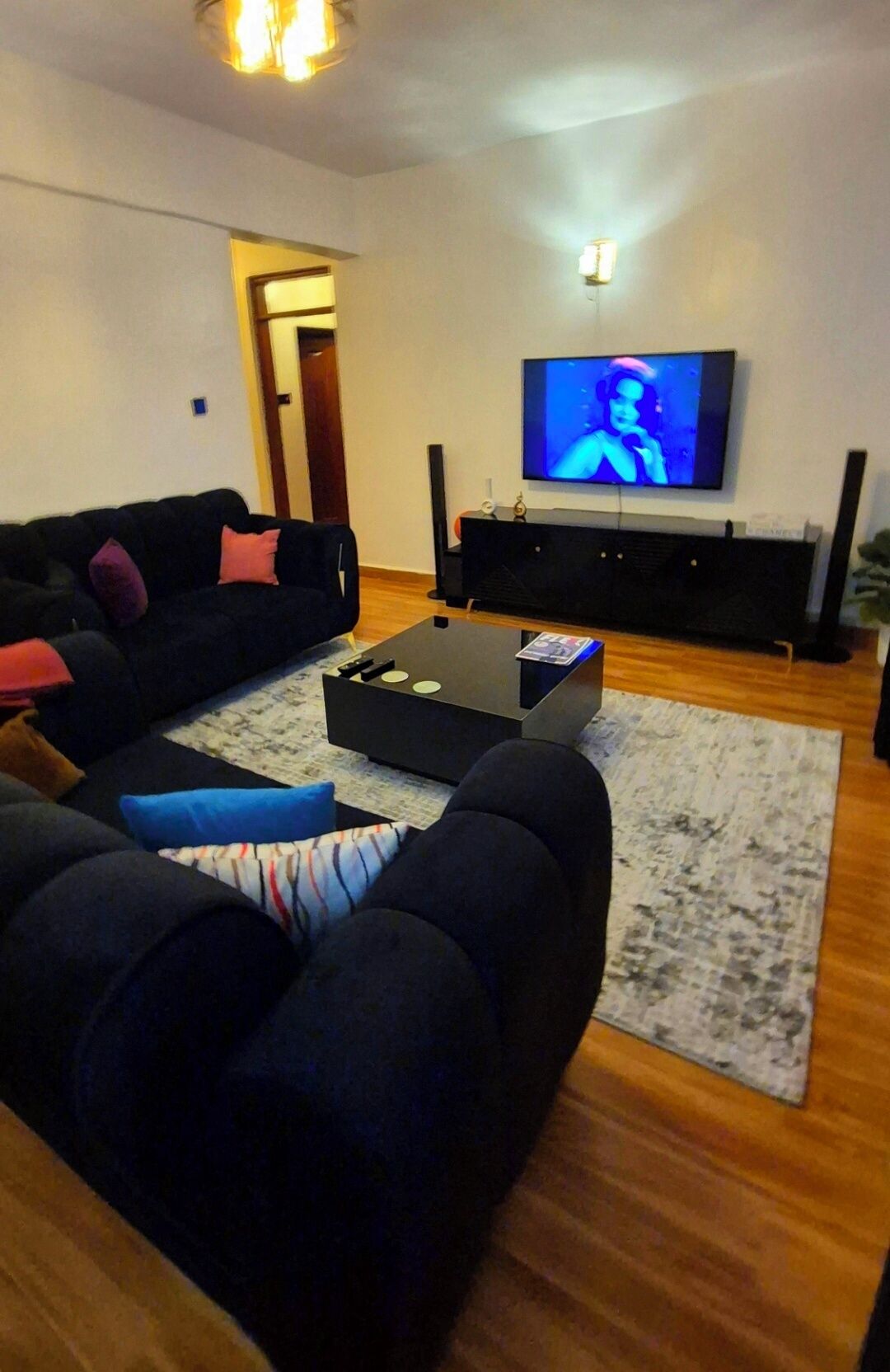 Ett vardagsrum med en svart soffa, ett soffbord och en platt-TV som är monterad på väggen.
