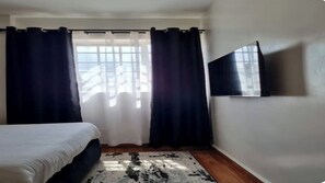 Une chambre à coucher avec un lit, un téléviseur à écran plat fixé au mur et une fenêtre avec des rideaux.