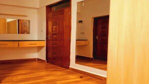 A room with wooden flooring, a wooden door, and a mirror on the wall.