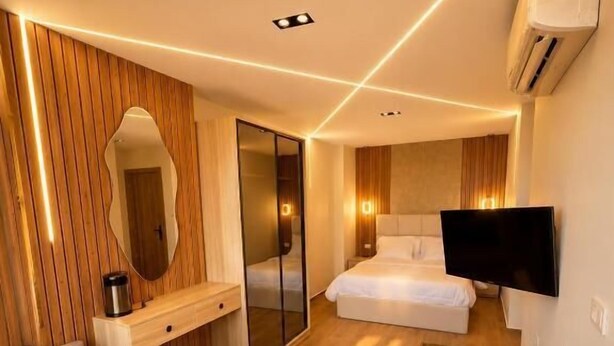 Quarto de hotel moderno com sofá, cama, TV e mini-geladeira.