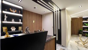 Uma área de recepção com um balcão preto, ripas de madeira vertical na parede e uma luminária moderna.