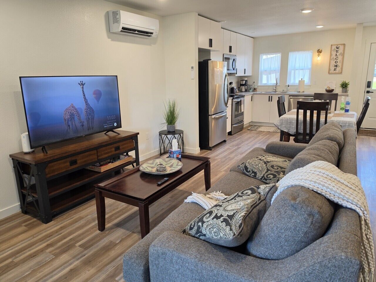 A living room with a TV, sofa, coffee table, and a kitchen in the background.