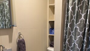 Et badeværelse med en hvid vask, et toilet, en brusekabine med et geometrisk mønster og et spejl over vasken.