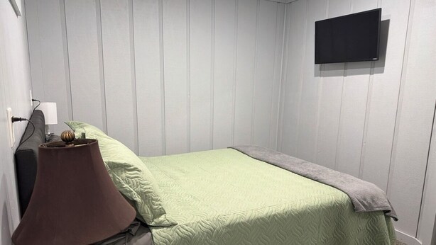Et soveværelse med en seng, en lampe og et fjernsyn på væggen.
