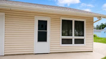 Una casa de un piso con fachada de color beige, una puerta delantera blanca y dos ventanas con cortinas.