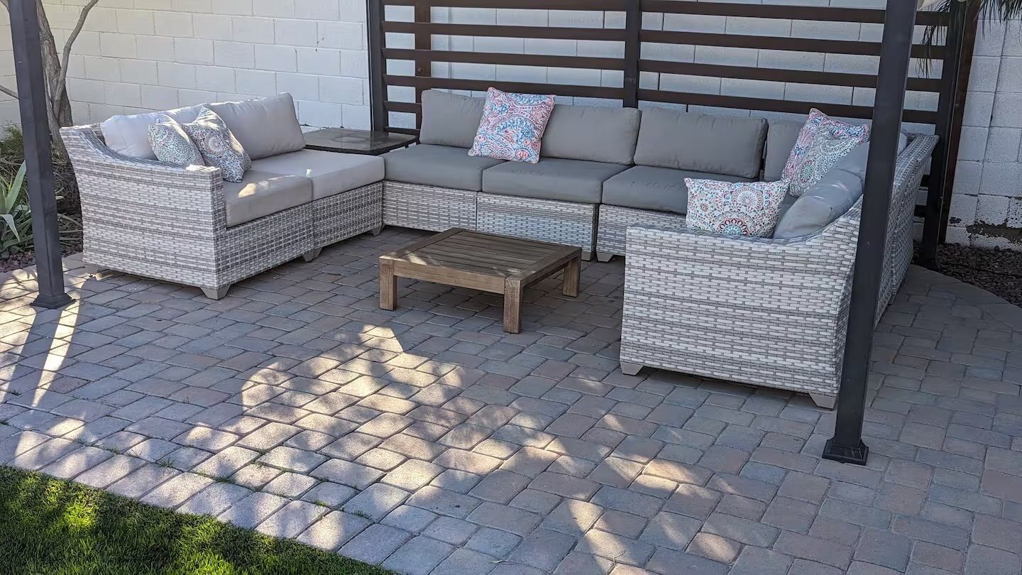 A wicker sectional sofa with cushions, a wooden coffee table, and a pergola structure.