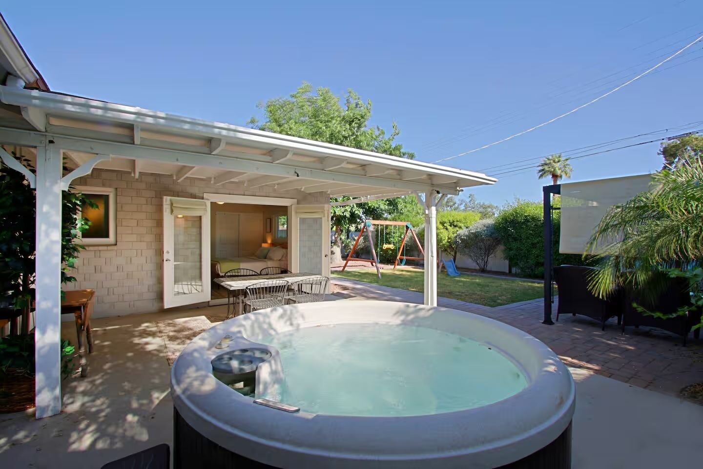 A backyard with a hot tub, a covered patio, a swing set, and a dining area.