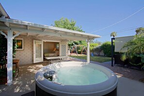 Een achtertuin met een hottub, een overdekt terras, een schommelset en een eethoek.