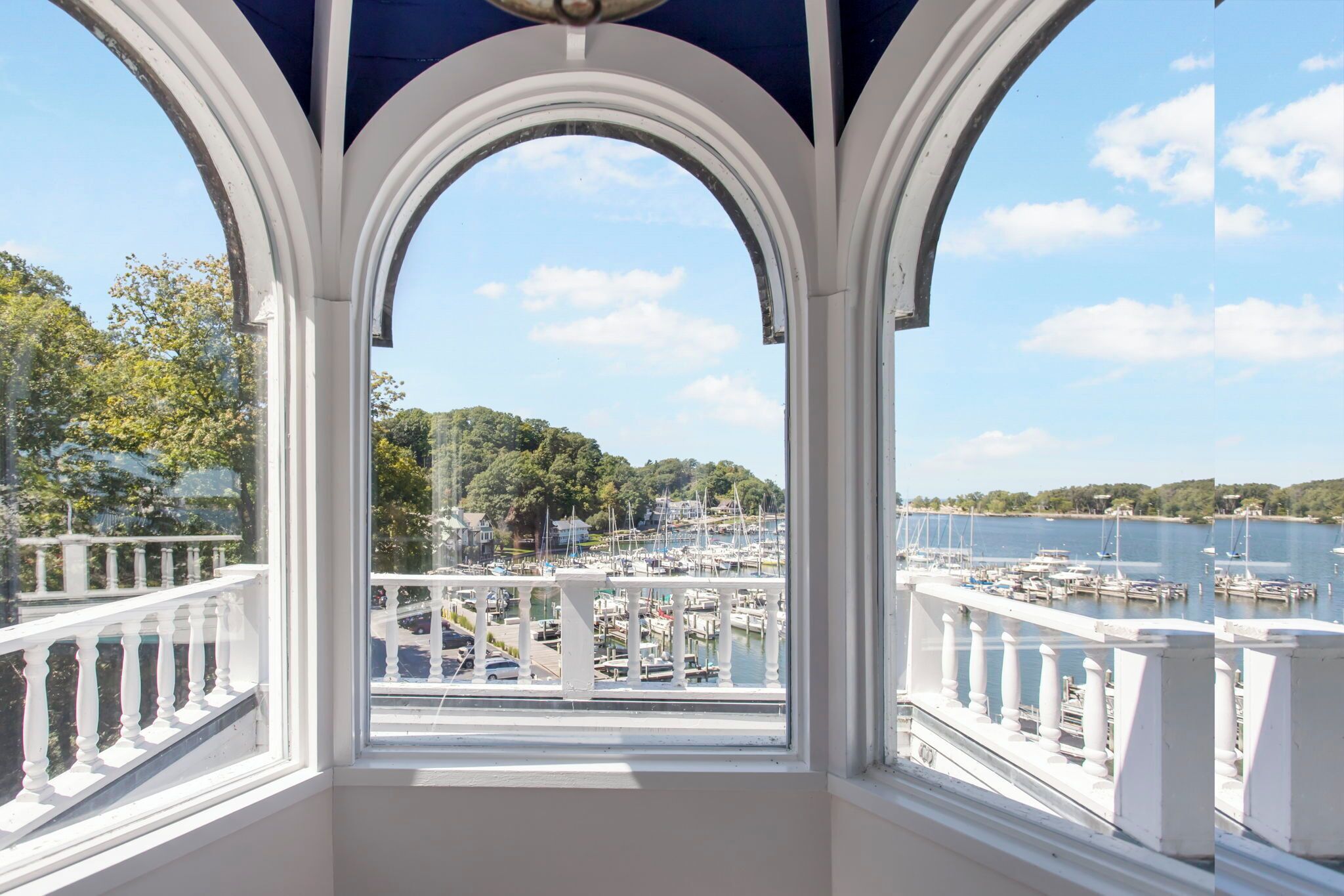 A covered balcony with a view of a marina and a forested hill.