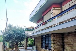 A two-story residential building with a balcony on the upper floor, a brick facade, and a tree in the background.