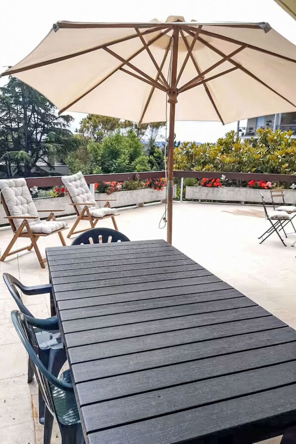 An outdoor seating area with a table and chairs, an umbrella, and a view of a garden with various plants and flowers.