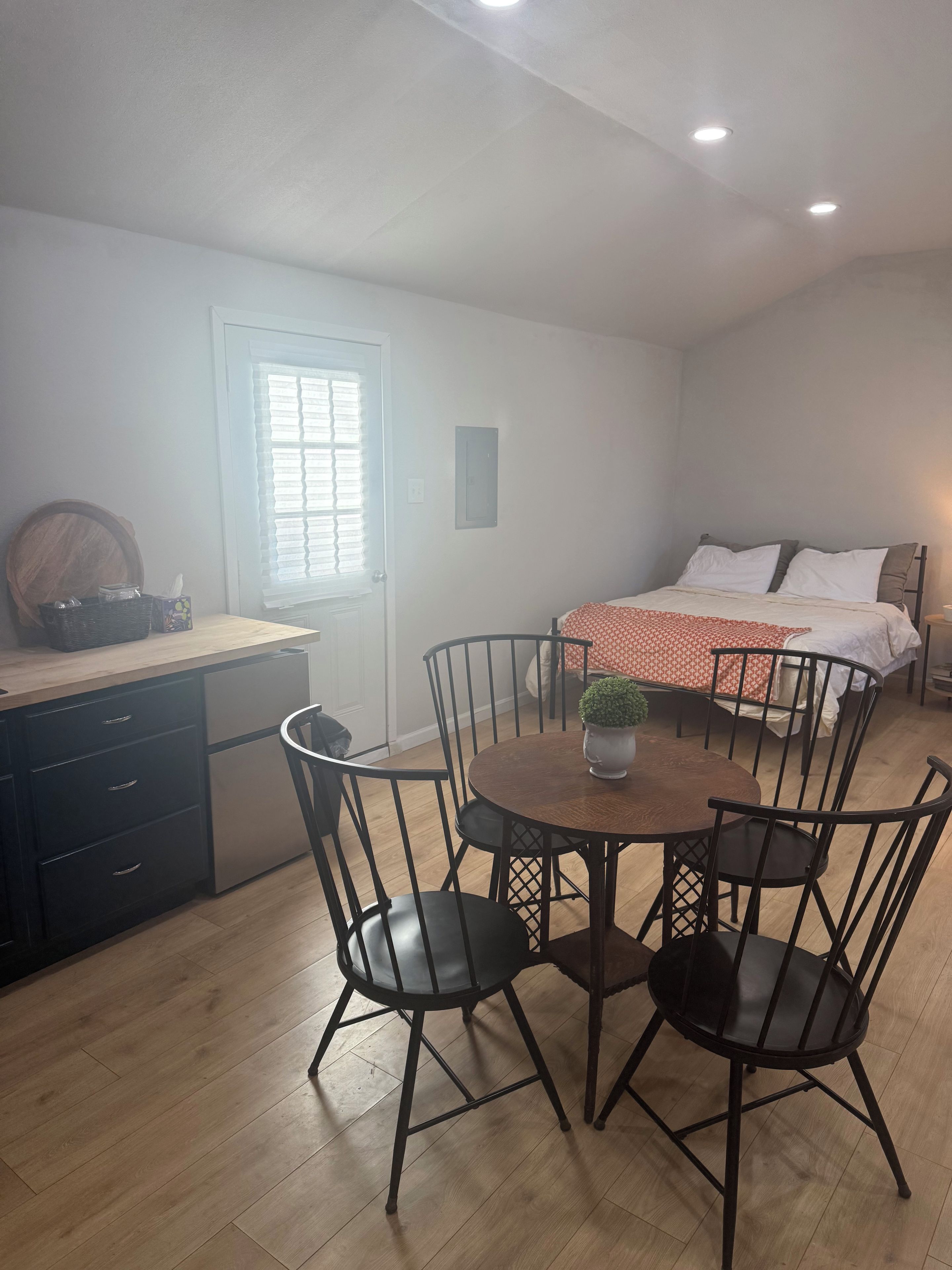 Une pièce comprenant une table à manger, des chaises, un lit, une fenêtre avec des stores et une porte.