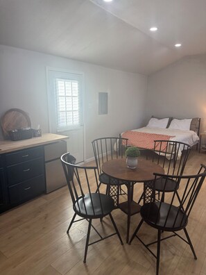A room with a dining table, chairs, a bed, a window with blinds, and a door. - Lakeside Hideaway, cabin with AC in cozy Brownwood, Walk to Water (Brownwood)