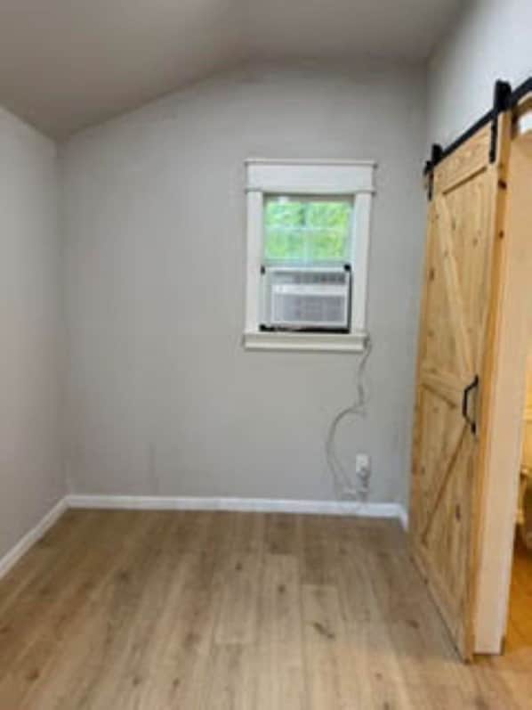 A room with a wooden floor, a window with an air conditioning unit, and a wooden door.