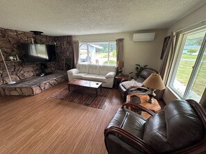 Ein Wohnzimmer mit Kamin aus Stein, einem Flachbildfernseher, einem weißen Sofa, einem braunen Ledersofa und einem Couchtisch aus Holz.