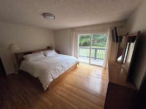 A bedroom with a wooden floor, a bed with white bedding, a nightstand, a lamp, and a view of a balcony with a railing. - Spacious 4-bedroom house near Jedidiah Smith State Park/Redwood National Park (Crescent City)