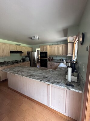 A kitchen with granite countertops, wooden cabinets, a refrigerator, an oven, and a coffee maker. - Spacious 4-bedroom house near Jedidiah Smith State Park/Redwood National Park (Crescent City)