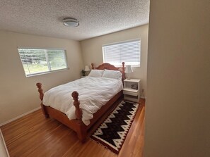 Un dormitorio con una cama de madera, dos mesitas de noche y un ventanal con persianas.