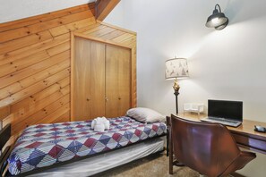 Ein Schlafzimmer mit Bett, Schreibtisch mit Laptop, Stuhl, Lampe und Kleiderschrank.