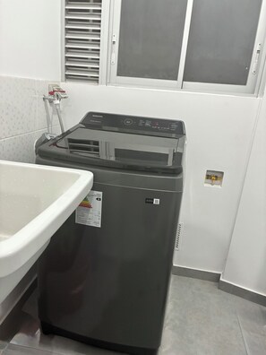 Eine kompakte, moderne Waschmaschine mit Bedienfeld, kleinem Fenster und Wasserzulaufschlauch.
