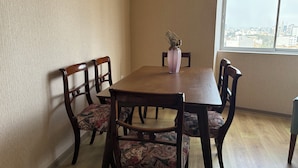 Comedor con mesa y sillas de madera, un jarrón con flores secas y vistas a la ciudad a través de una ventana.