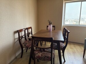 Ein Essbereich mit einem Holztisch und Stühlen, einer Vase mit getrockneten Blumen und Blick auf die Stadt durch ein Fenster.