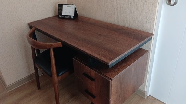 Un escritorio de madera con un calendario, una silla y una unidad de cajones.