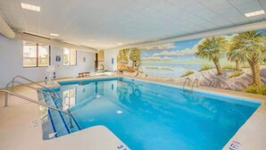 Ein Hallenbad mit Wandgemälde von einer Strandlandschaft, einem Rettungsschwimmerstuhl und einem Fenster mit Jalousien.