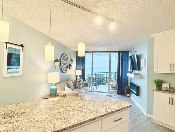 A modern kitchen with a granite countertop, a dining area with a sofa, and a balcony with a view. - Top-Shelf Terrace w/ Oceanview from the 11th Floor (Myrtle Beach)