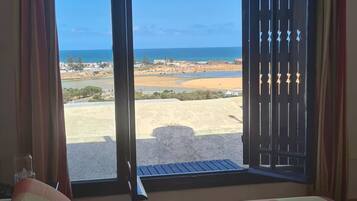 A bedroom with a large bed, a view of the beach, and a balcony with a railing.