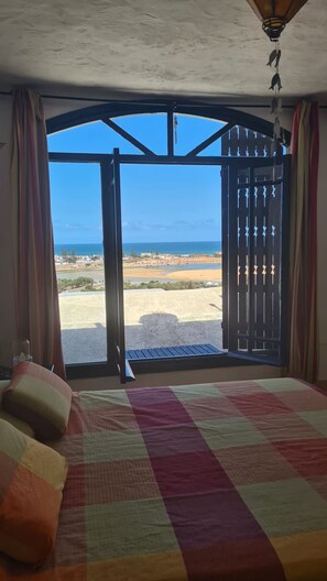 A bedroom with a large bed, a view of the beach, and a balcony with a railing.