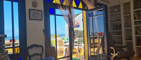 Een kamer met uitzicht op het strand, een eethoek met stoelen en tafels, en een boekenkast.