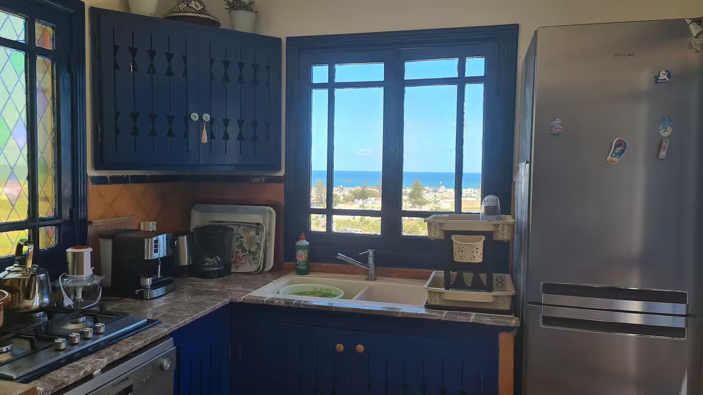 A kitchen with a view of the sea, a refrigerator, a stove, and a sink.