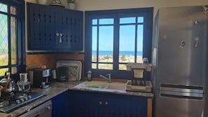 A kitchen with a view of the sea, a refrigerator, a stove, and a sink.