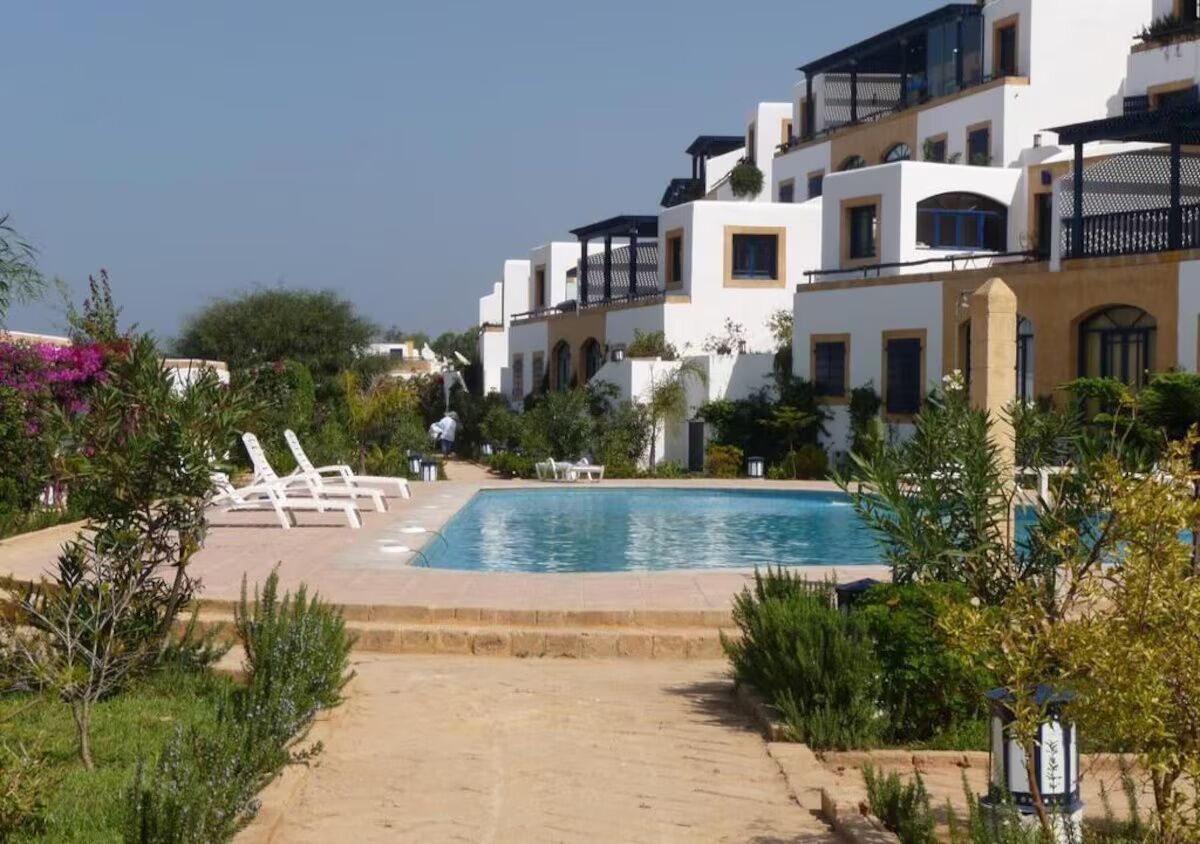 A pool area with lounge chairs and a clear sky.
