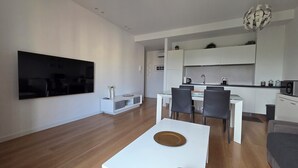 A modern living room with a flat-screen TV, a dining area with a white table and chairs, and a kitchen with white cabinets and appliances. - For your vacation in Catania, just a few hundred meters from downtown. (Catania)