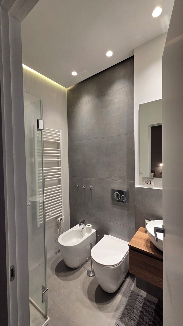 Een moderne badkamer met een douchecabine van glas, een toiletbril, een wc en een wastafelmeubel met een wastafel.