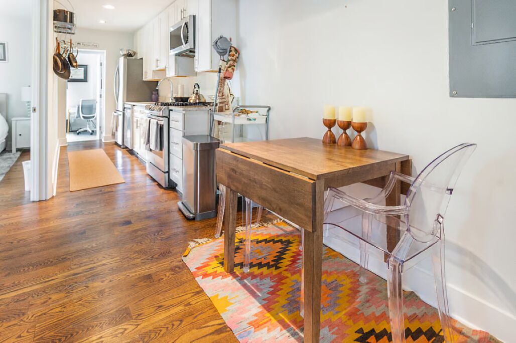 A modern kitchen with wooden flooring, a dining table with chairs, and a colorful rug.