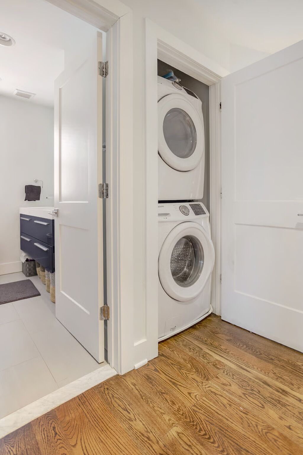 A laundry room with a front-loading washer and dryer, a small cabinet, and a door leading to another room.