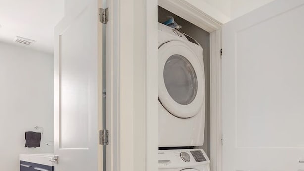 A laundry room with a front-loading washer and dryer, a small cabinet, and a door leading to another room. - Lovely 2-bedroom condo with parking near H Street / Union Market (Washington)