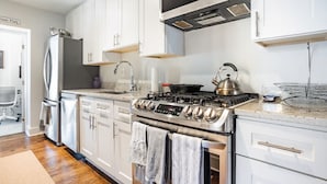 A modern kitchen with stainless steel appliances, white cabinetry, and a wood floor. - Lovely 2-bedroom condo with parking near H Street / Union Market (Washington)