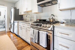 A modern kitchen with stainless steel appliances, white cabinetry, and a wood floor. - Lovely 2-bedroom condo with parking near H Street / Union Market (Washington)