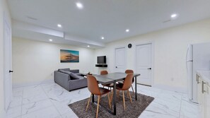 Ein modernes Wohnzimmer mit Sofa, Esstisch, Stühlen, einem Flachbildfernseher und einem Gemälde an der Wand.