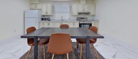 Une cuisine de taille réduite avec des meubles blancs, une table à manger avec des chaises et un réfrigérateur.