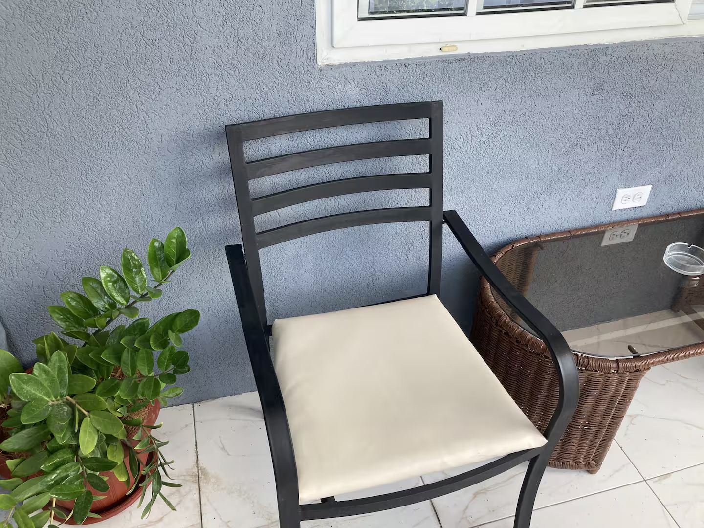 A chair with a cushioned seat and backrest, positioned next to a potted plant and a wicker basket on a tiled floor.