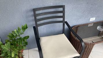 A chair with a cushioned seat and backrest, positioned next to a potted plant and a wicker basket on a tiled floor.