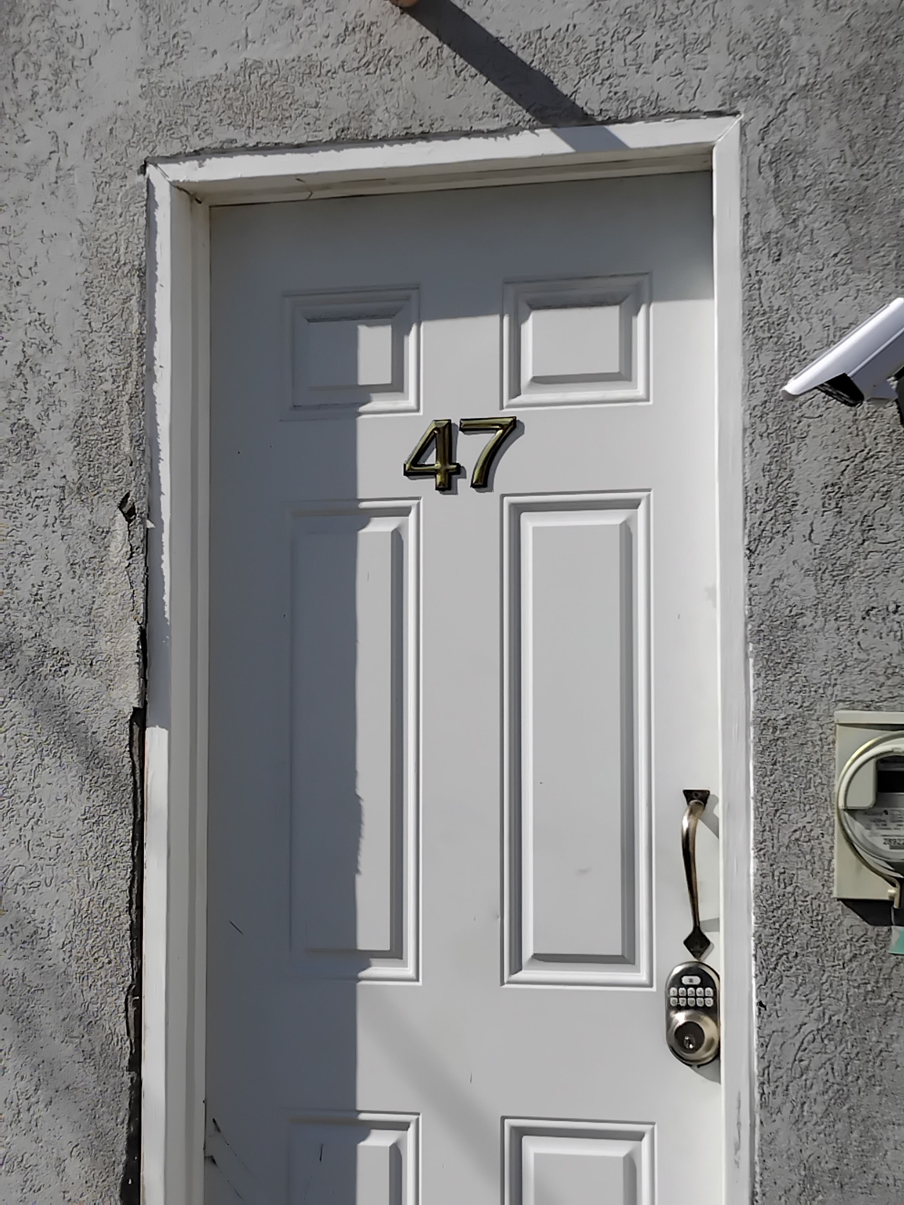 A white door with the number 47, a doorbell, and a security camera mounted on the wall.