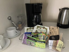 Una encimera de cocina con una cafetera, un hervidor y una bandeja de bolsitas de té y condimentos.