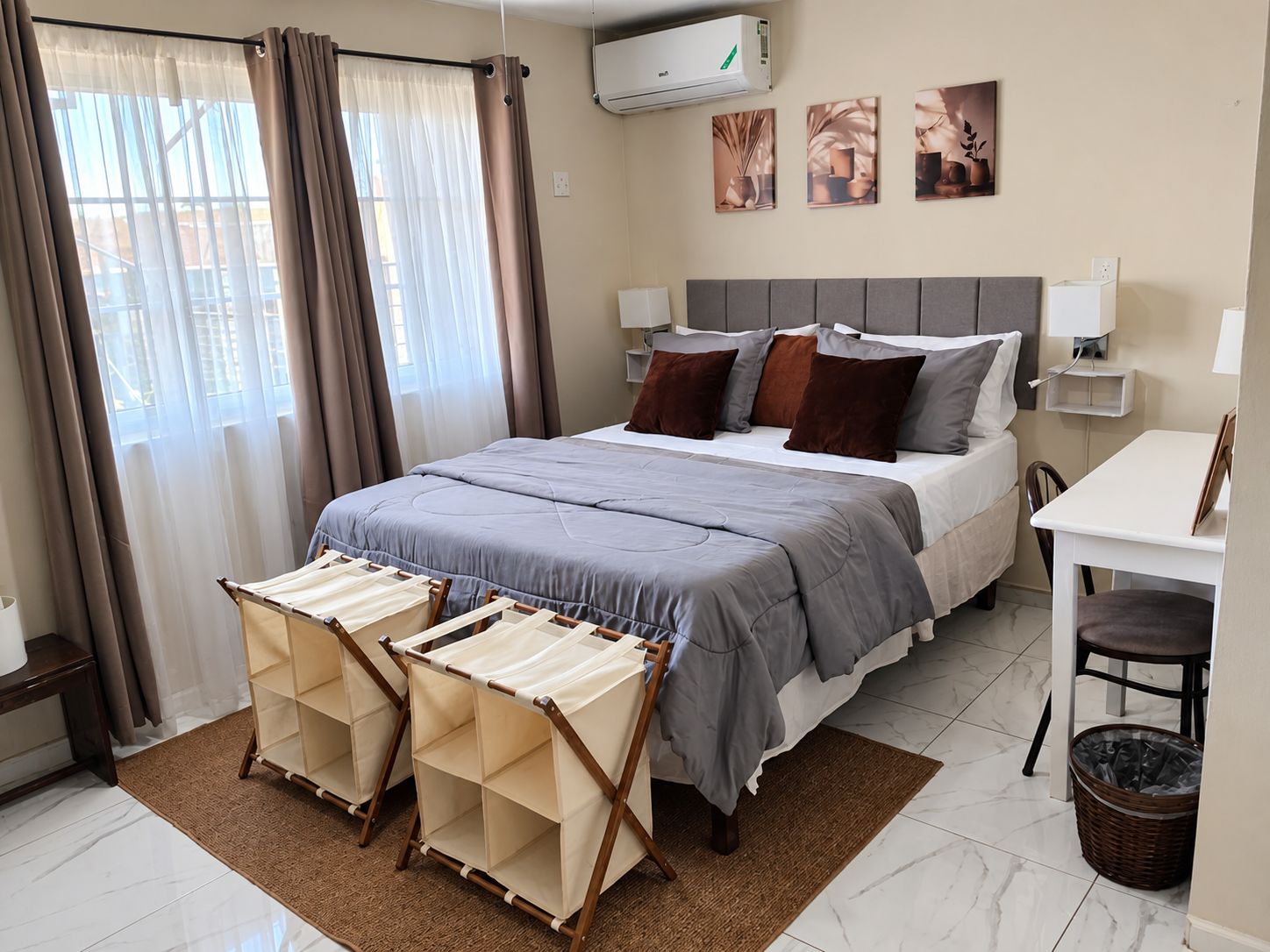Habitación de hotel con cama, mesitas de noche, escritorio, silla, ventana con cortinas y una obra de arte en la pared.