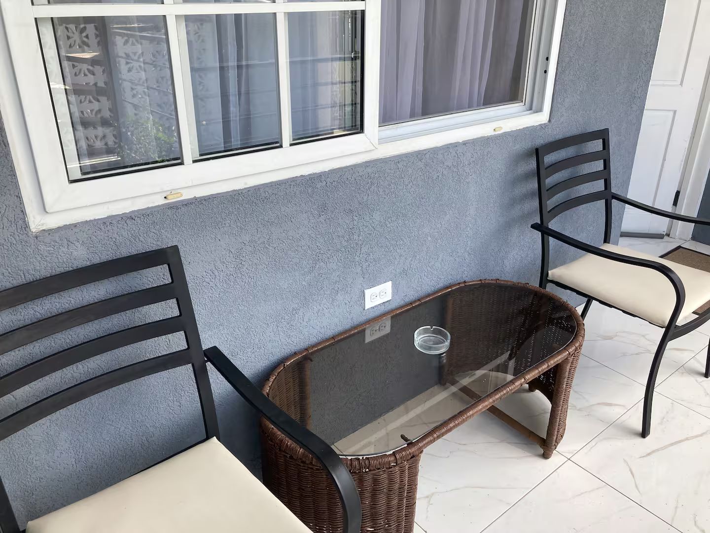 A room with two wicker chairs, a glass table, and a window with curtains.